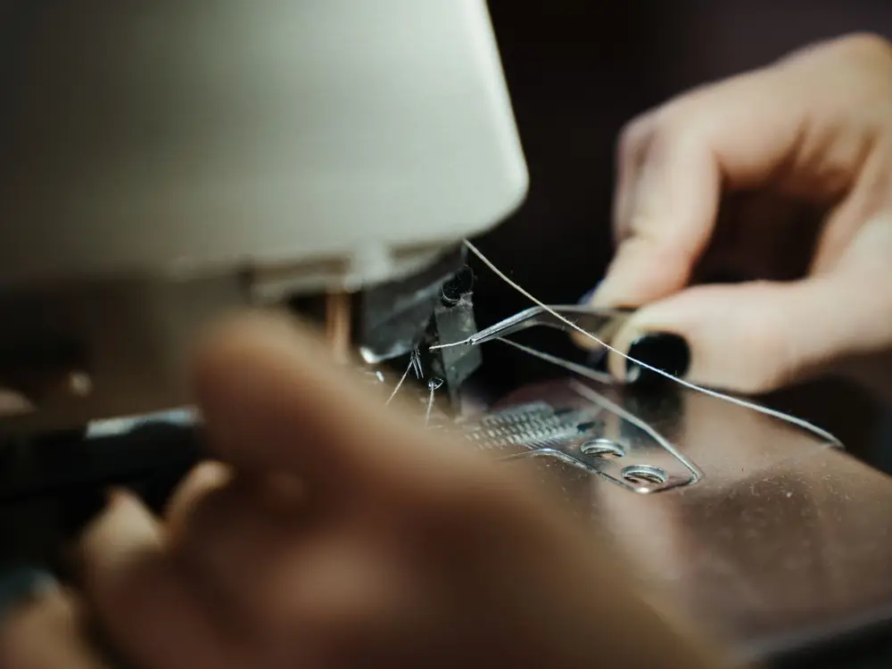 Close-up of hands guiding thread through a sewing machine needle